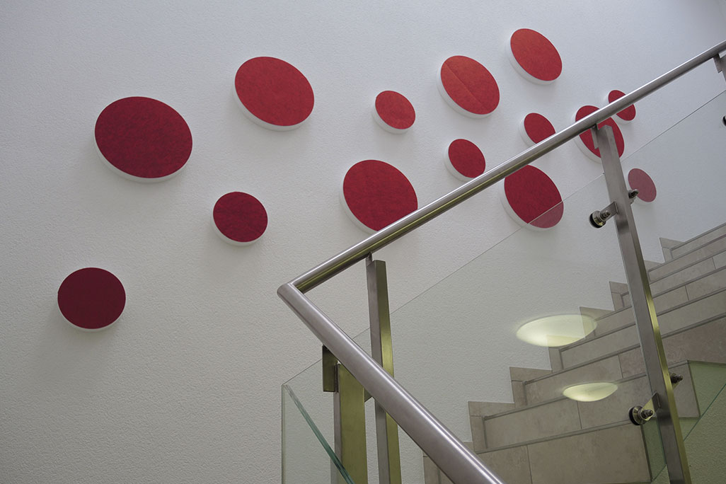 14 Schallabsorber in Form eines Kreises (soni ELEMENT CIRCLE) in der Farbe Rot auf einer weißen Wand in einem modernen Treppenhaus angebracht.