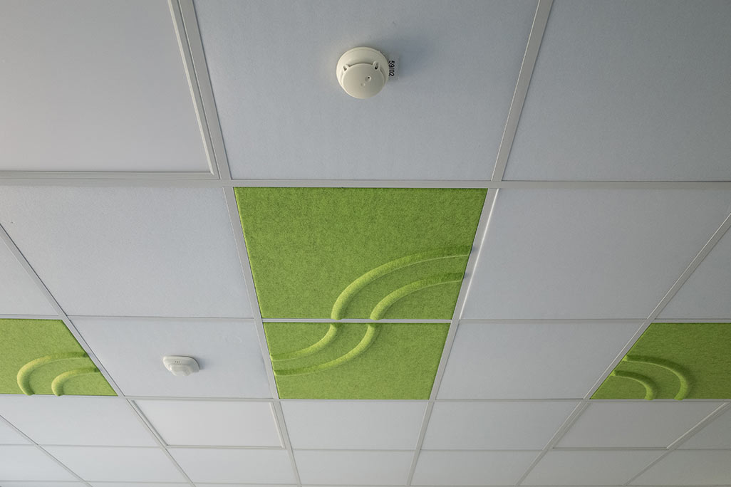 Ausschnitt einer handelsüblichen Rasterdecke mit eingelegten Akustikabsorbern soni COMFORT SD in Weiß und soni COLOR Design in Grün.