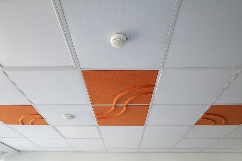 Ausschnitt einer handelsüblichen Rasterdecke mit eingelegten Akustikabsorbern soni COMFORT SD in Weiß und soni COLOR Design in Orange.