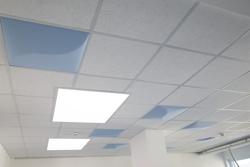 Ausschnitt einer handelsüblichen Rasterdecke mit eingelegten Akustikabsorbern soni COMFORT SD in Weiß und soni COLOR Design in Blau.