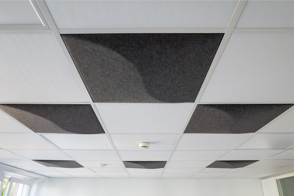 Ausschnitt einer handelsüblichen Rasterdecke mit eingelegten Akustikabsorbern soni COMFORT SD in Weiß und soni COLOR Design in Anthrazit.