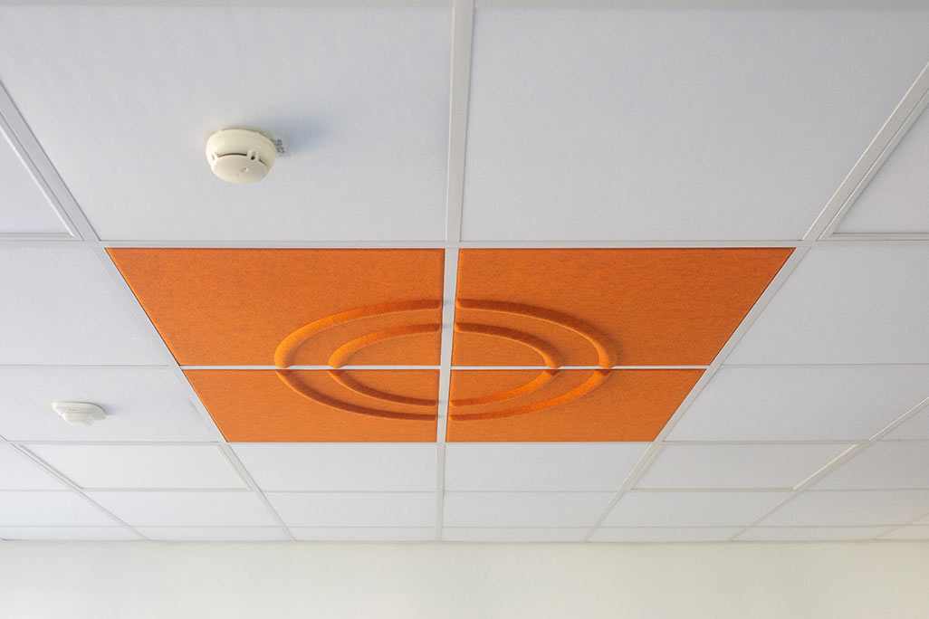 Ausschnitt einer handelsüblichen Rasterdecke mit eingelegten Akustikabsorbern soni COMFORT SD in Weiß und soni COLOR Design in Orange.
