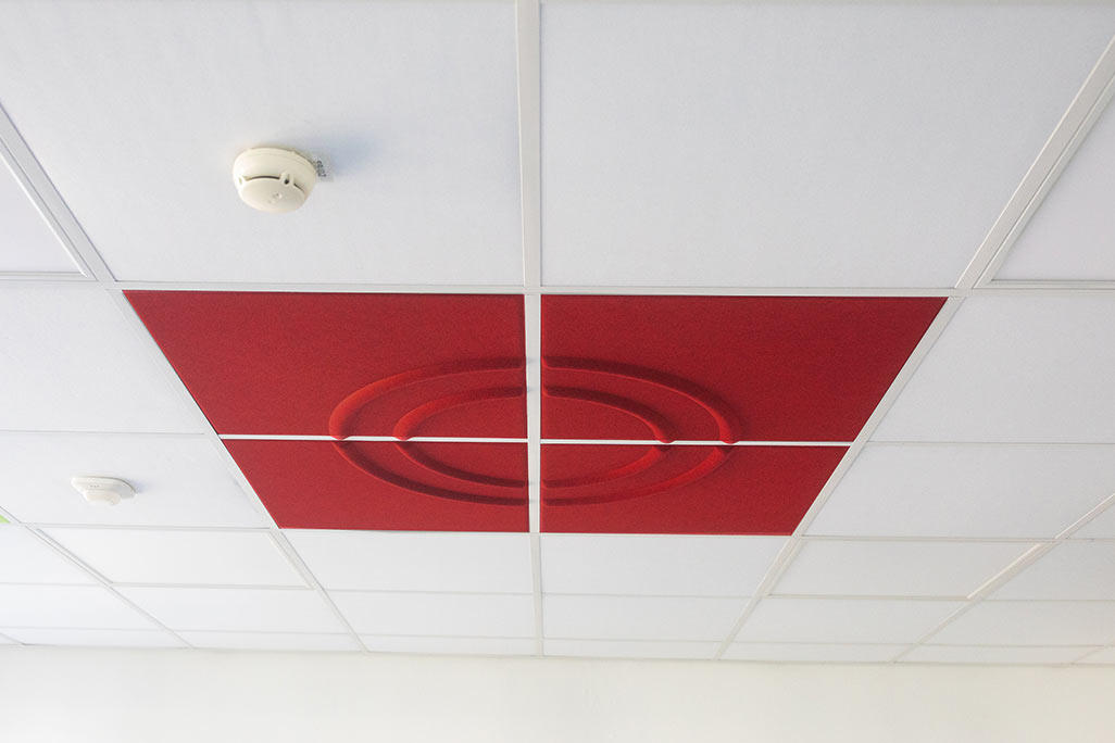 Ausschnitt einer handelsüblichen Rasterdecke mit eingelegten Akustikabsorbern soni COMFORT SD in Weiß und soni COLOR Design in Rot.