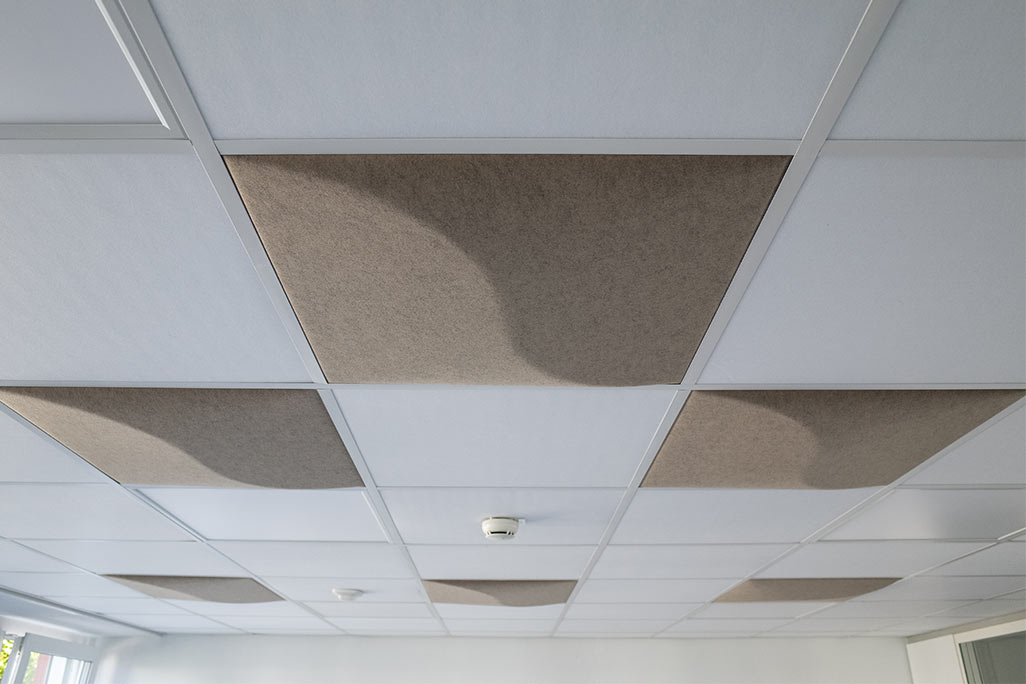 Ausschnitt einer handelsüblichen Rasterdecke mit eingelegten Akustikabsorbern soni COMFORT SD in Weiß und soni COLOR Design in Beige.