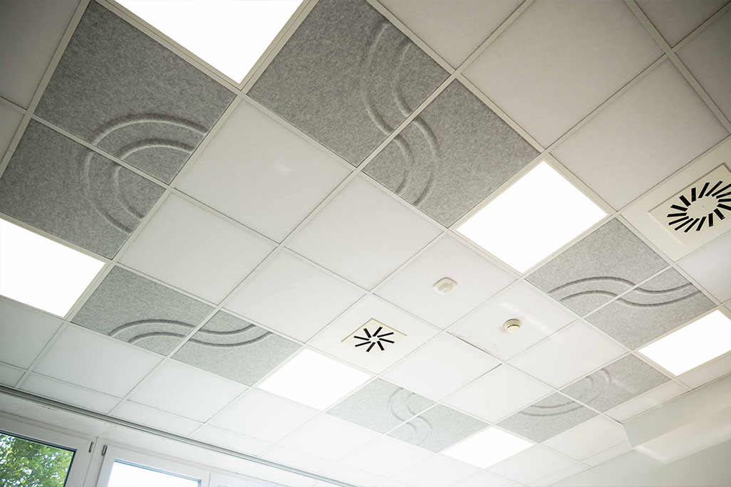 Ausschnitt einer handelsüblichen Rasterdecke mit eingelegten Akustikabsorbern soni COMFORT SD in Weiß und soni COLOR Design in Hellgrau.