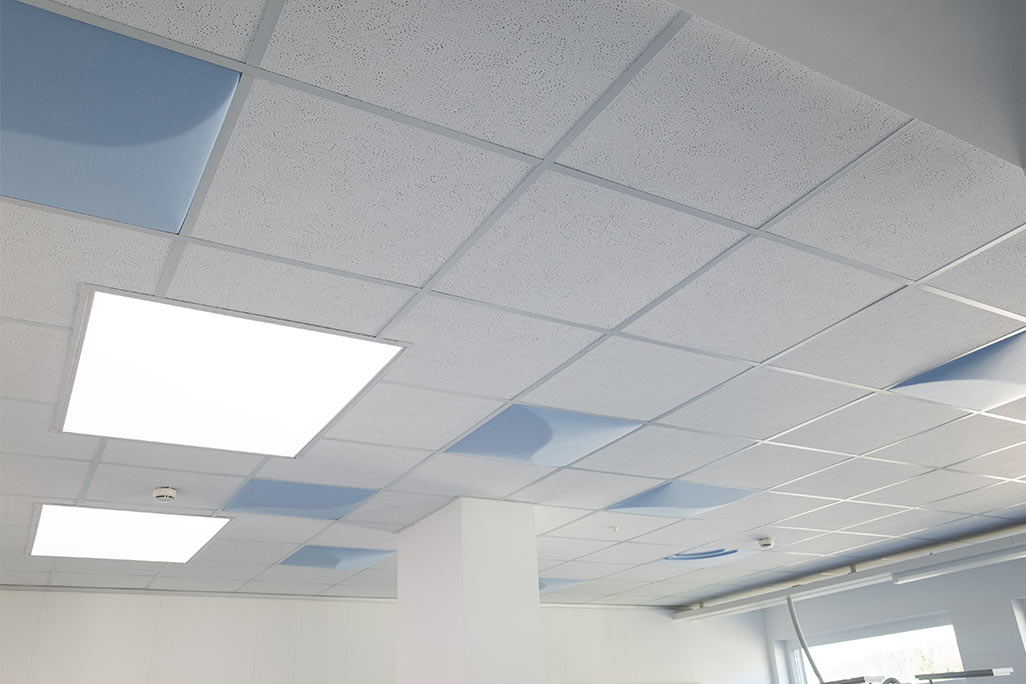 Ausschnitt einer handelsüblichen Rasterdecke mit eingelegten Akustikabsorbern soni COMFORT SD in Weiß und soni COLOR Design in Blau.