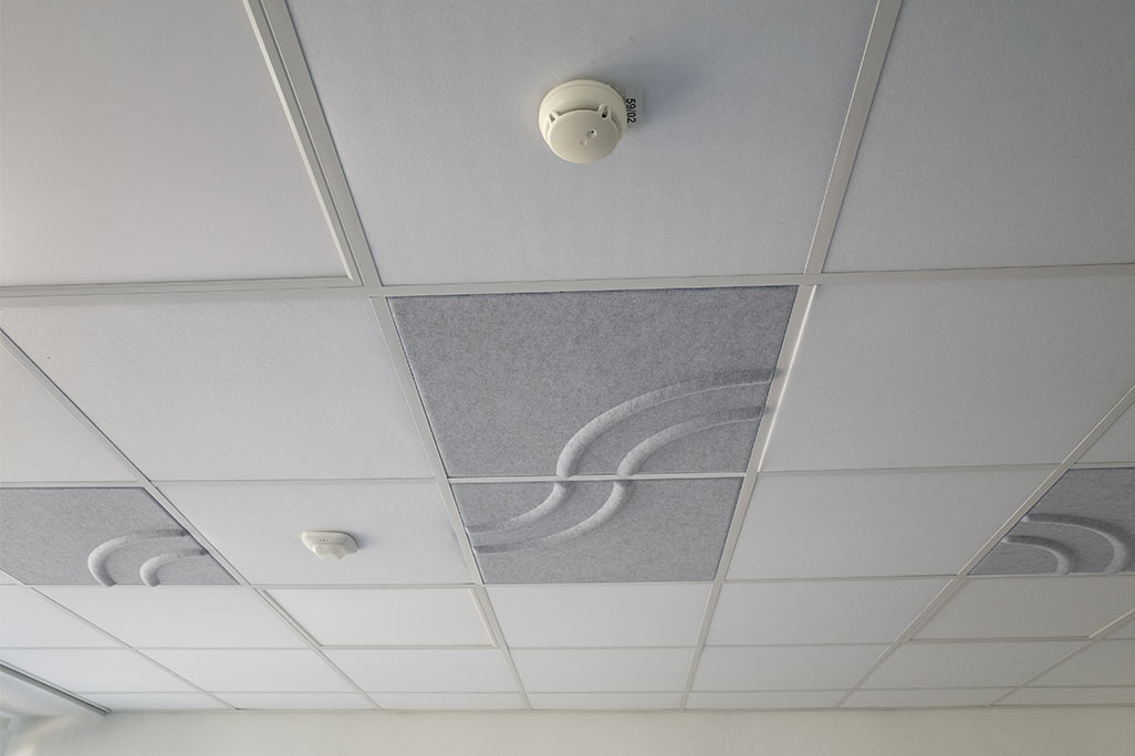 Ausschnitt einer handelsüblichen Rasterdecke mit eingelegten Akustikabsorbern soni COMFORT SD in Weiß und soni COLOR Design in Hellgrau.