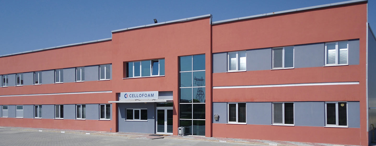 Vue du bâtiment de l'entreprise Cellofoam, un grand bâtiment d'entreprise rouge, autour duquel se trouvent des arbres verts.