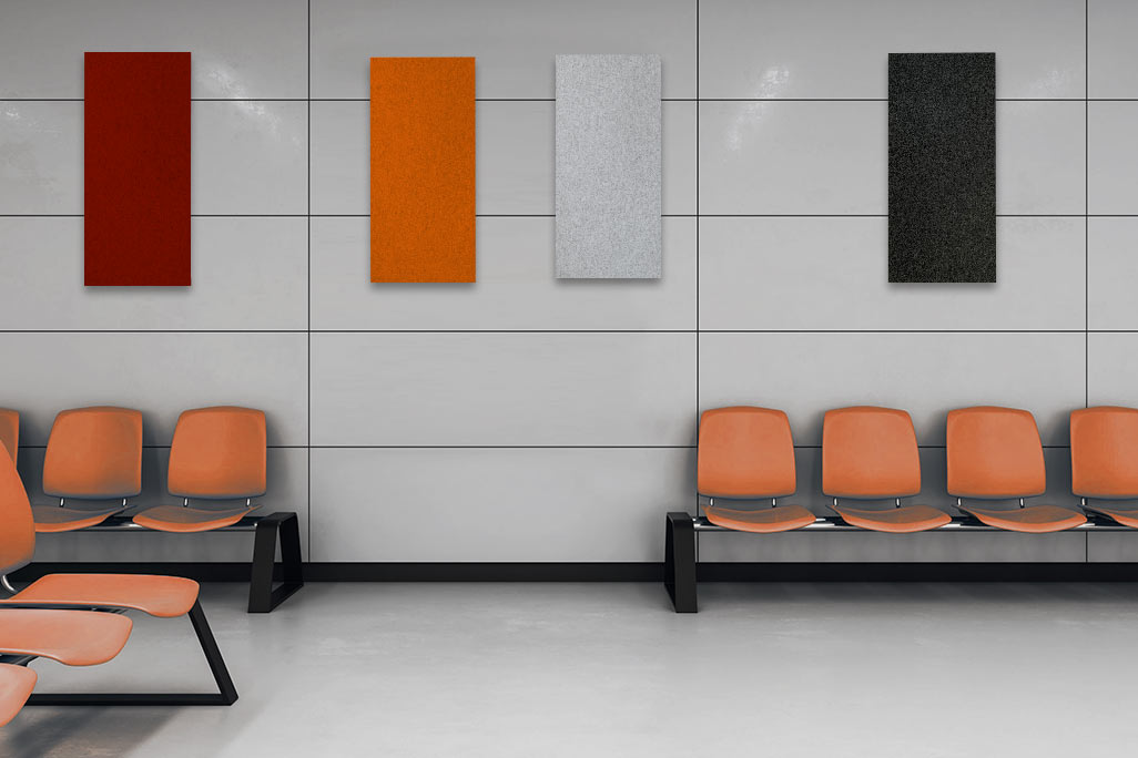 Warteraum mit orangefarbigen Stühlen und einer Wand, die vier rechteckige Akustikelemente in Rot, Orange, Hellgrau und Anthrazit zeigt