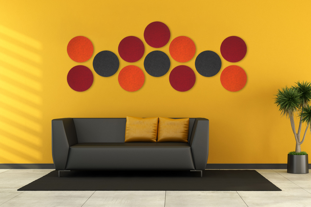 12 farbige Schallabsorber in Form eines Kreises (soni ELEMENT CIRCLE) auf einer gelben Wand in einem modernen Wohnzimmer mit schwarzem Ledersofa angebracht.